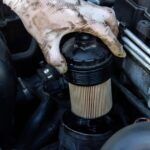 A person examining a car engine with a hose, suggesting issues with a clogged fuel filter.
